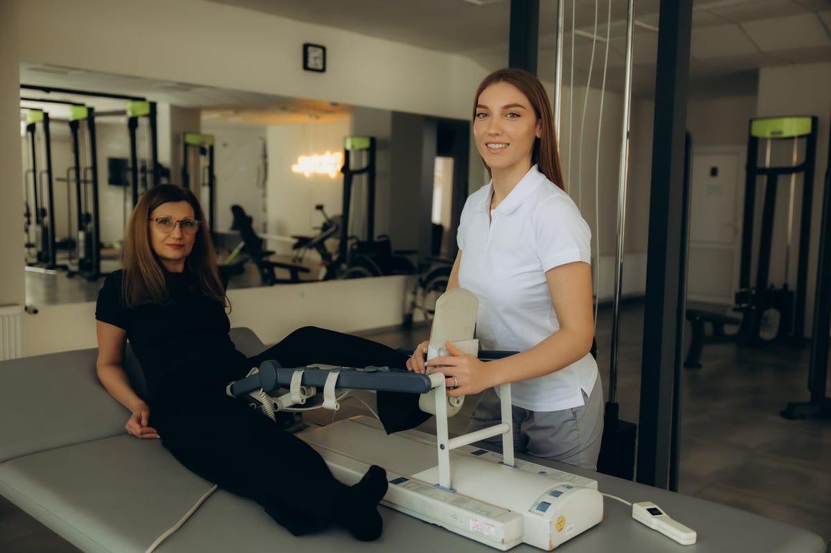 A patient receiving physiotherapy with a continuous passive motion machine while a therapist assists